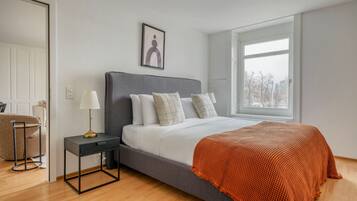 A modern bedroom with a large bed, a bedside table, a lamp, and a window.