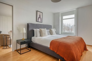 Een moderne slaapkamer met een groot bed, een nachtkastje, een lamp en een raam.