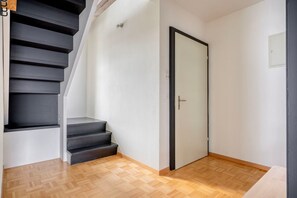 Un escalier menant à une pièce dotée d’une porte, d’un plancher en bois et d’un interrupteur sur le mur.