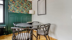 Un'area pranzo con un tavolo rotondo, quattro sedie, una parete decorata con un motivo floreale, una porta verde e un'opera d'arte astratta incorniciata.