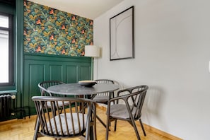 Een eetgedeelte met een ronde tafel, vier stoelen, een decoratieve wand met bloemenmotief, een groene deur en een lijst met abstracte kunst.