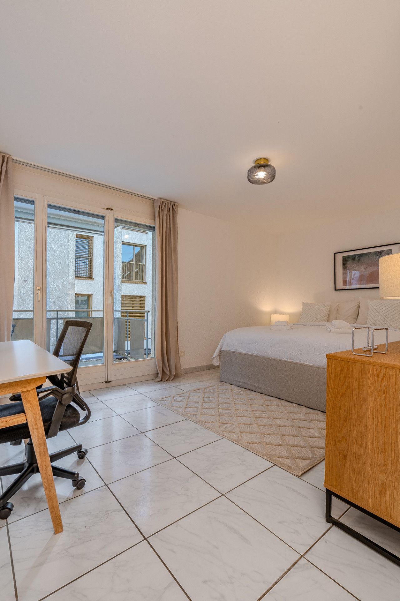 A hotel room with a bed, a desk, a chair, and a window with curtains.