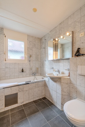 Een badkamer met een bad, wastafel, toilet en spiegel.