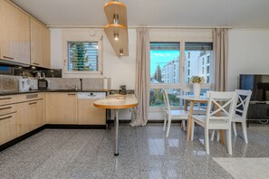 Une cuisine moderne dotée de plans de travail en granit, d’armoires en bois et d’un coin repas avec une table ronde et des chaises blanches.