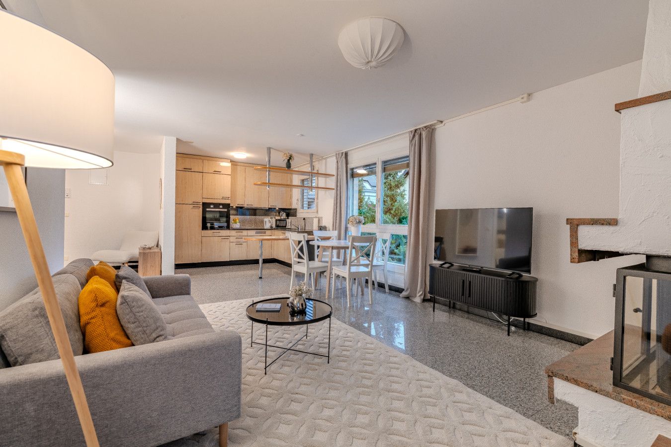 Ein modernes Wohnzimmer mit einem grauen Sofa, einem runden Couchtisch und einem Fernseher.