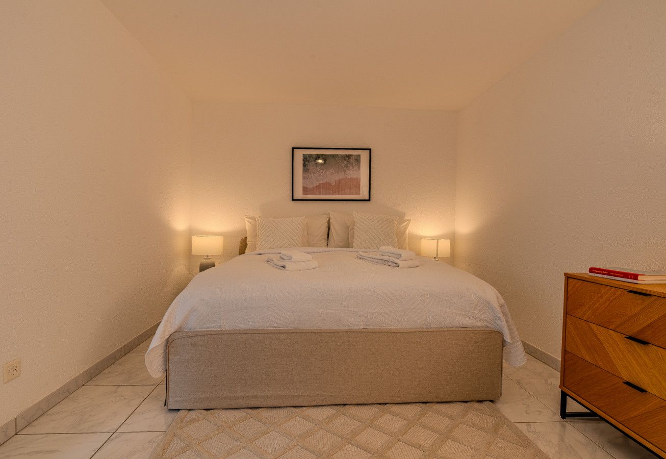 A bedroom with a bed, bedside lamps, a nightstand, a dresser, and a framed picture on the wall.