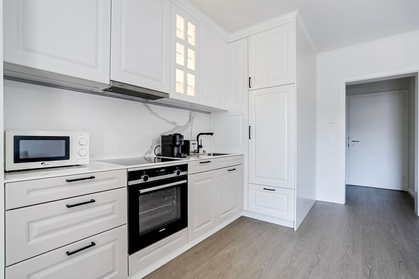 Eine moderne Küche mit weißen Schränken, einem eingebauten Backofen, einer Mikrowelle und einer Kaffeemaschine.