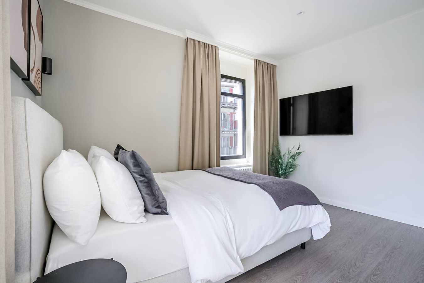 A modern bedroom with a bed, curtains, a TV, and a window.