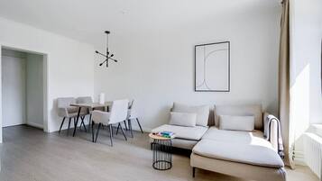 Ein modernes Wohnzimmer mit einer Couch, einem Esstisch mit Stühlen, einem Couchtisch und einer Pendelleuchte.