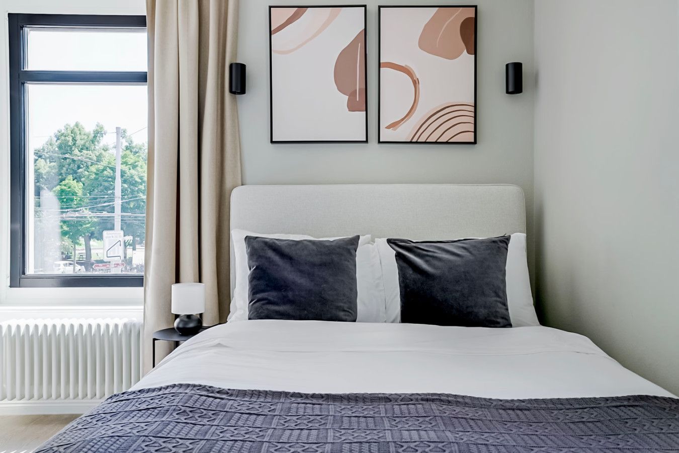 Ein Hotelzimmer mit einem Bett, einem Fenster mit Vorhängen, einem Heizkörper und zwei Wandleuchten.