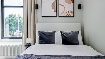Ein Hotelzimmer mit einem Bett, einem Fenster mit Vorhängen, einem Heizkörper und zwei Wandleuchten.