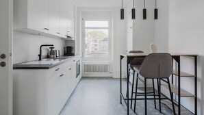 Une cuisine moderne équipée d’un four encastré, d’une bouilloire et d’une machine à café. Un coin repas avec une table et des chaises est également à disposition.
