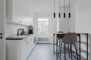 Een moderne keuken met een ingebouwde oven, waterkoker en koffiezetapparaat. Er is een eethoek met een tafel en stoelen.