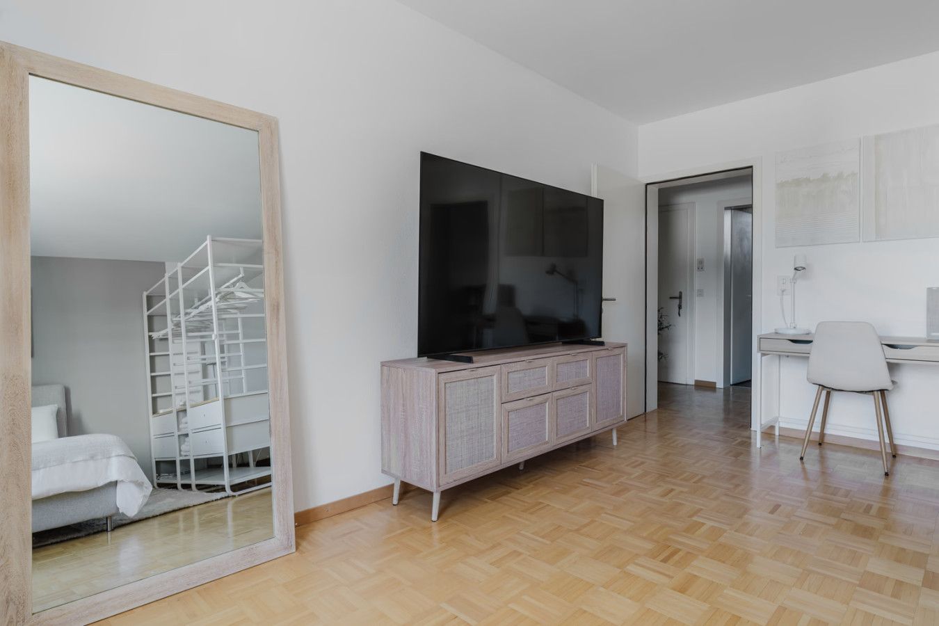Ein modernes Wohnzimmer mit einem großen Spiegel, einem Flachbildfernseher, einem Holzschrank und einem Schreibtisch mit Stuhl.