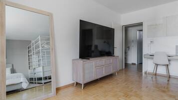 Ein modernes Wohnzimmer mit einem großen Spiegel, einem Flachbildfernseher, einem Holzschrank und einem Schreibtisch mit Stuhl.