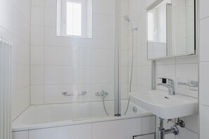 Een moderne badkamer met een douchecabine van glas, een witte badkuip en een wastafel met spiegel.