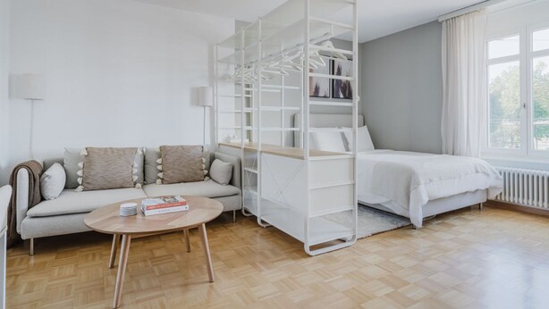 Un salon moderne avec un canapé, une table basse et une étagère blanche où sont rangés des vêtements.