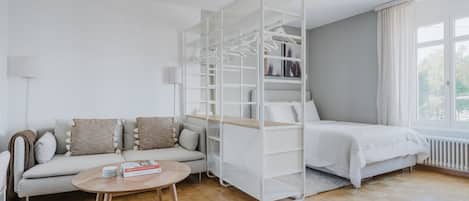 A modern living room with a sofa, coffee table, and a white shelving unit with clothes.