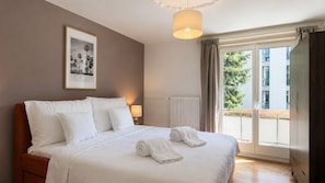 A hotel room with a large bed, a framed picture on the wall, a window with curtains, and a view of the outside.