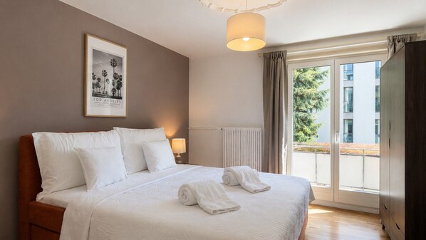 A hotel room with a large bed, a framed picture on the wall, a window with curtains, and a view of the outside.