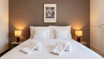 Une chambre d’hôtel avec un grand lit, deux lampes de chevet, un tableau encadré au mur et des serviettes roulées posées sur le lit.
