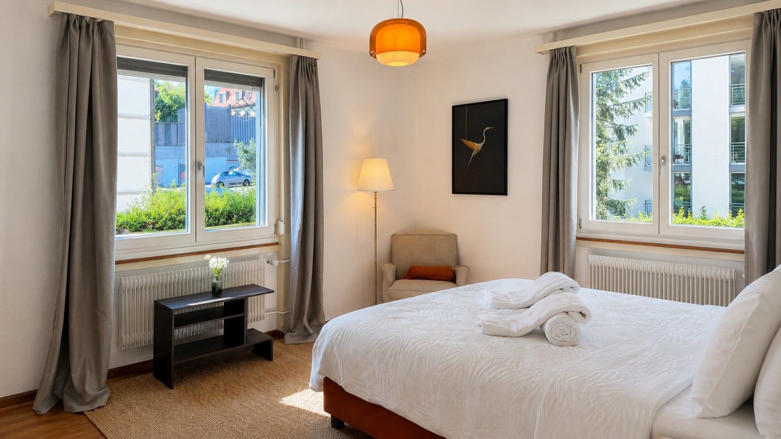 Une chambre d’hôtel avec un lit, un bureau, une chaise, une lampe et une fenêtre avec des rideaux.