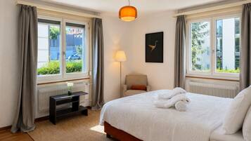 Une chambre d’hôtel avec un lit, un bureau, une chaise, une lampe et une fenêtre avec des rideaux.