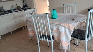 Un área de comedor con una mesa cubierta con un mantel estampado, rodeada de sillas de metal blanco.