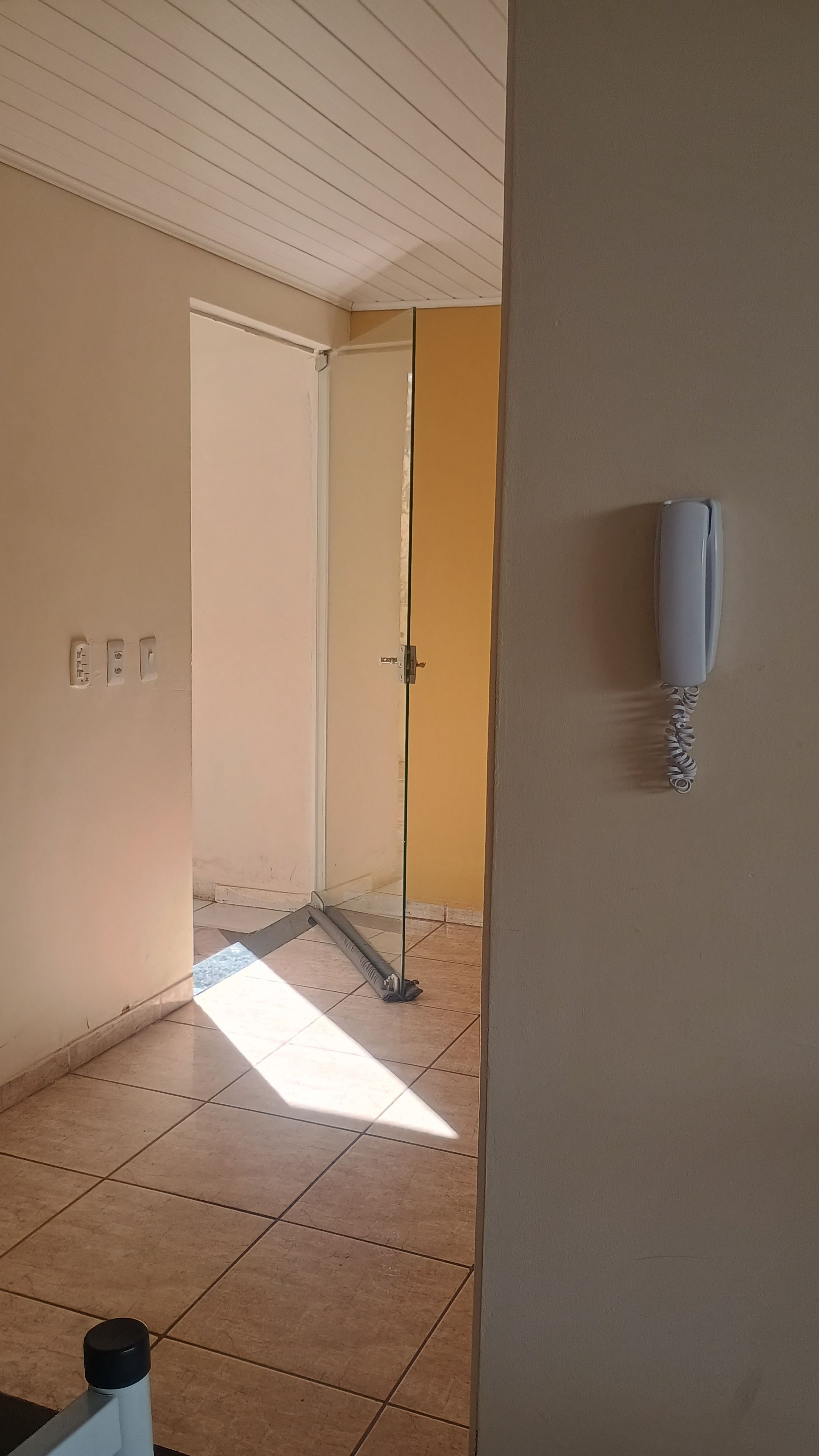A room with a tiled floor, a glass door leading to another room, and a wall-mounted telephone.