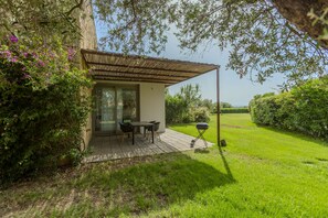 Eine Terrasse mit Tisch, Stühlen, einem Grill und Blick auf ein grünes Feld.