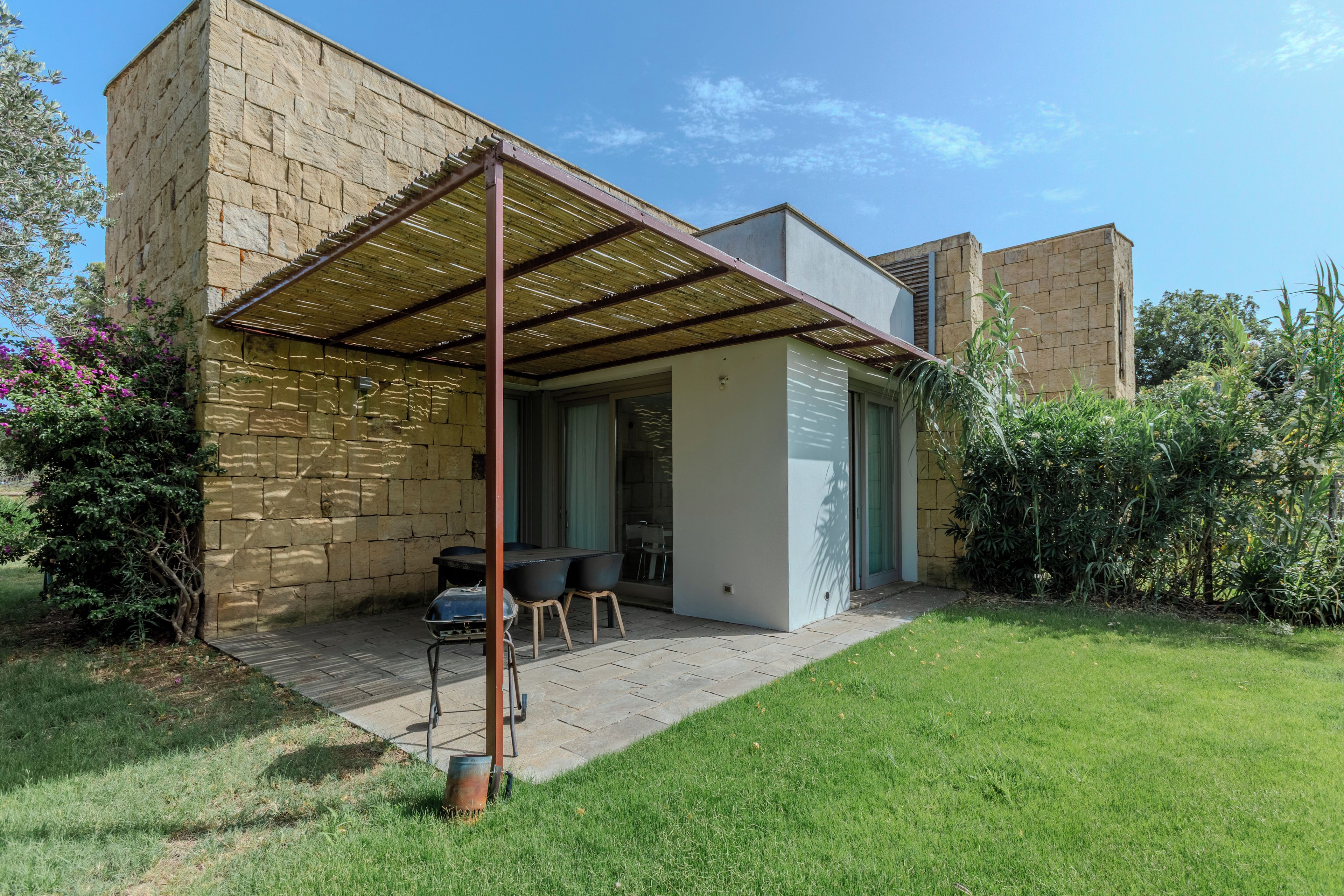 Una casa moderna con un porche cubierto, paredes de piedra y un patio con césped.
