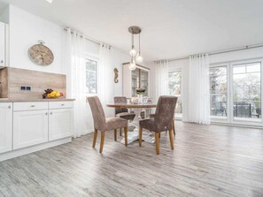 A modern kitchen with white cabinetry, a wooden countertop, and a dining area with two chairs and a table. - Park Residence Am Hafen 23 - \"viento\" (Zingst)