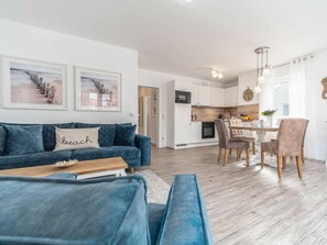 Ein modernes Wohnzimmer mit einem blauen Sofa, einem Holztisch und einem Essbereich mit Tisch und Stühlen.