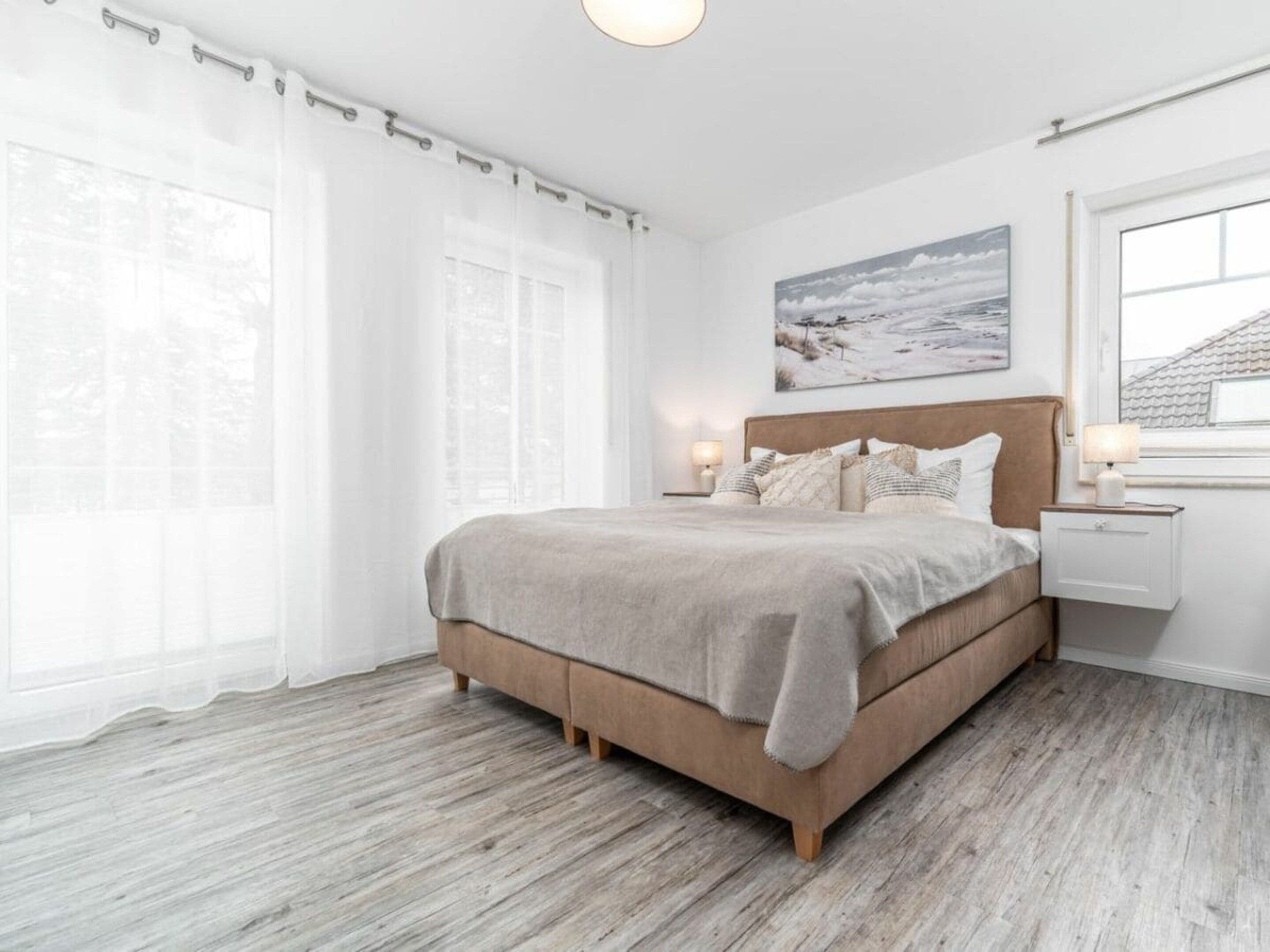 Ein Schlafzimmer mit Bett, Nachttischen, einem Fenster mit Vorhängen und einem Bild an der Wand.