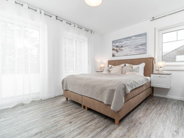A bedroom with a bed, bedside tables, a window with curtains, and a painting on the wall. - Park Residence Am Hafen 23 - \"viento\" (Zingst)