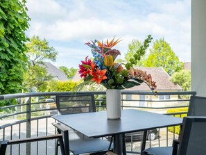 Ein Balkon mit Tisch und Stühlen, einer Blumenvase und Blick auf Häuser und Grünflächen.