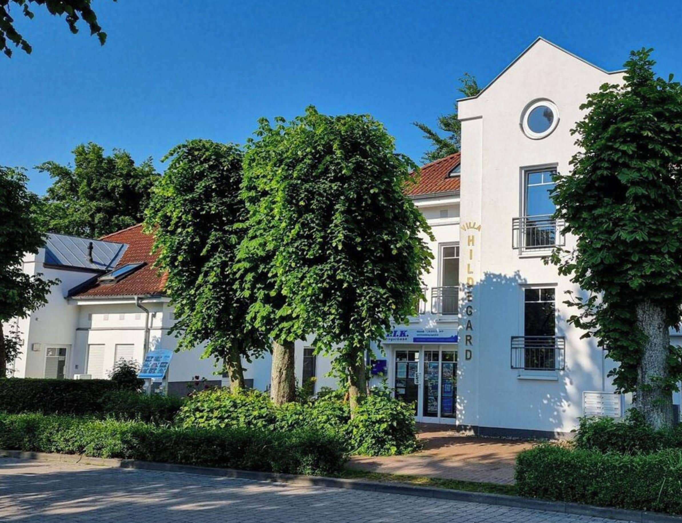 Ein modernes Gebäude mit weißer Fassade, einem runden Fenster im oberen Stockwerk und einem Schild mit dem Namen 'Hilda' auf der rechten Seite.