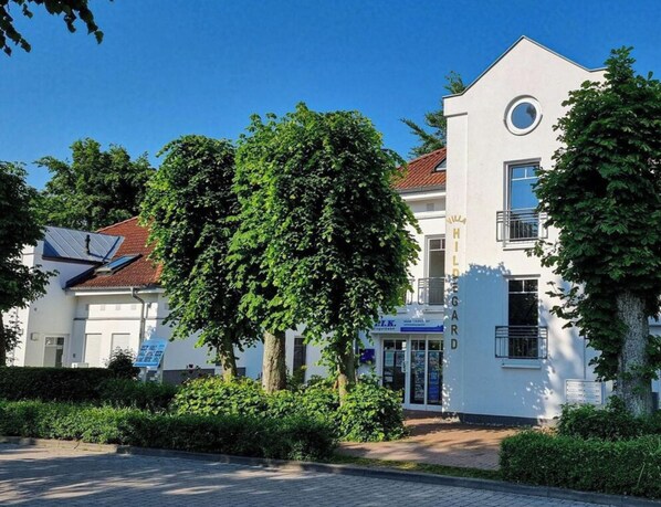 Ein modernes Gebäude mit weißer Fassade, einem runden Fenster im oberen Stockwerk und einem Schild mit dem Namen 'Hilda' auf der rechten Seite.