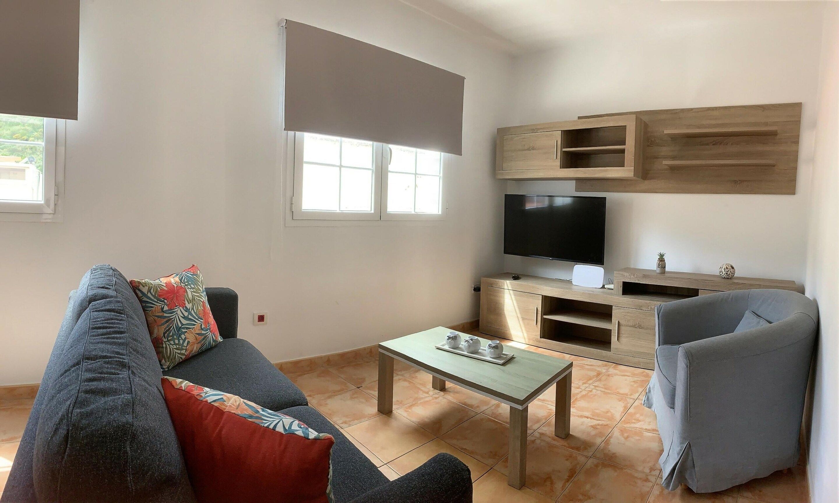 Een woonkamer met een bank, salontafel, televisie en een stoel.