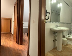 A bathroom with a sink, toilet, and shower. There is a white chair in the adjacent room. - Charming 2-bedroom Artenara Home (Valleseco)
