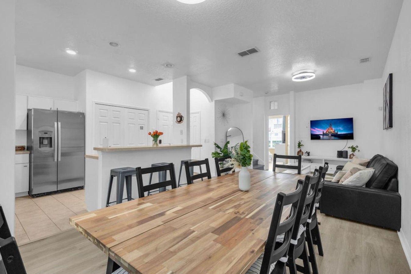 Een moderne keuken met een roestvrijstalen koelkast, een zithoek met een houten tafel en stoelen, en een woonkamer met een zwarte bank en een flatscreen televisie.