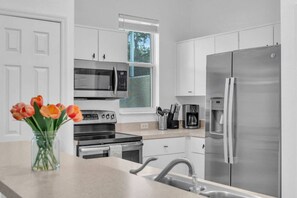 Cozinha moderna com eletrodomésticos de aço inoxidável, janela com vista e um vaso de tulipas sobre o balcão.