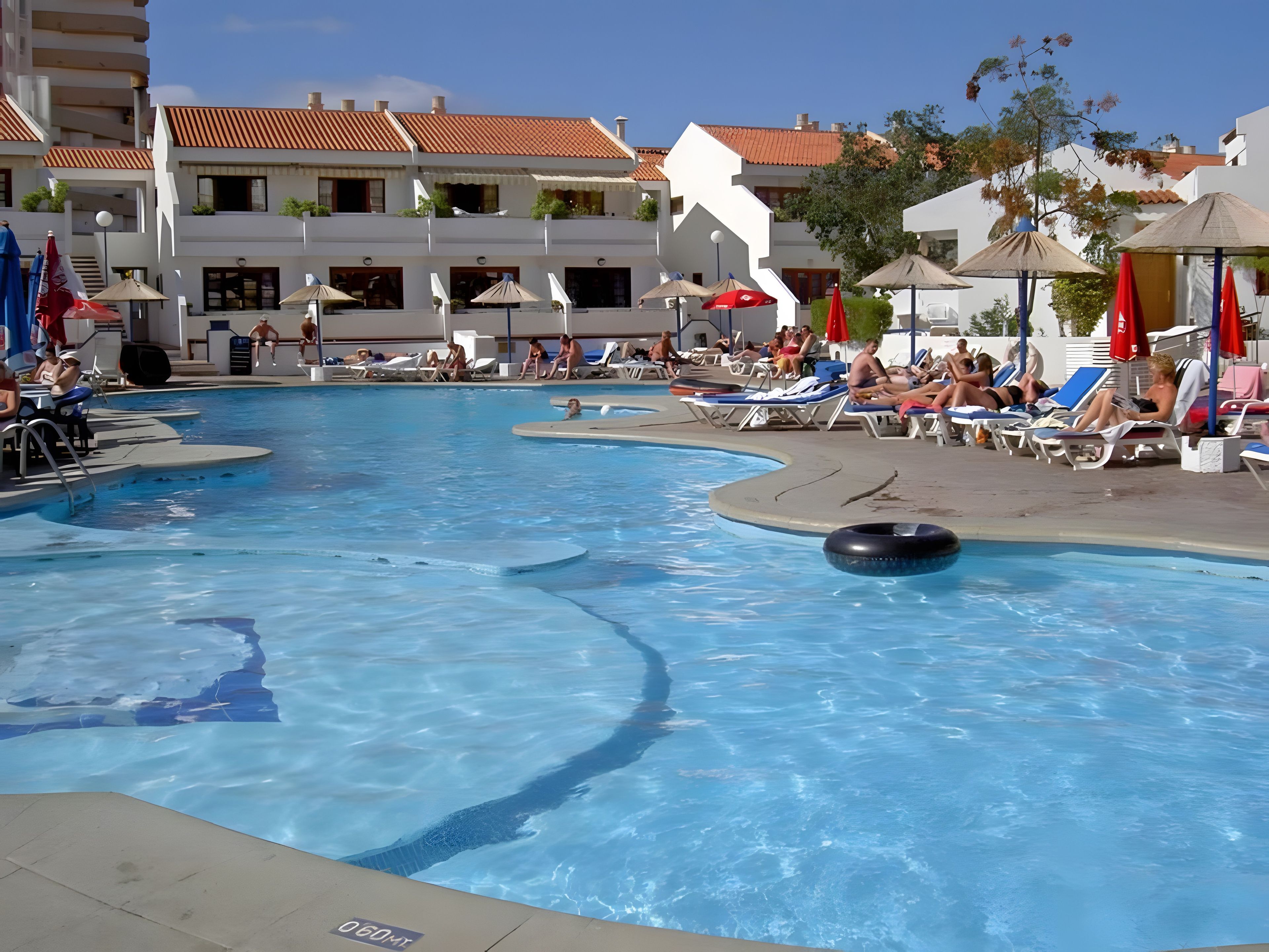 A swimming pool with lounge chairs and umbrellas, surrounded by buildings with balconies.