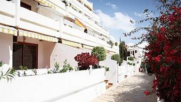 Un bâtiment blanc doté de nombreux balcons, d’une allée pavée et de plantes à fleurs rouges.