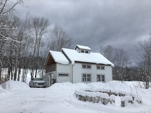 Una casa de dos pisos con techo nevado y un coche estacionado al frente.