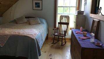 A bedroom with a bed, a rocking chair, a dresser, and a window with a view of greenery.