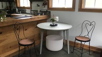 A kitchen with a wooden countertop, a sink, and a window above the sink. There are two chairs with heart-shaped backs and a small table with a potted plant.