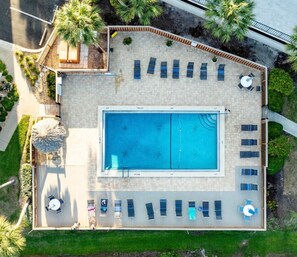 Ein rechteckiger Pool mit einer gefliesten Liegefläche, umgeben von Liegestühlen und Sonnenschirmen, sowie eine kleine Sitzecke mit Tisch und Stühlen.