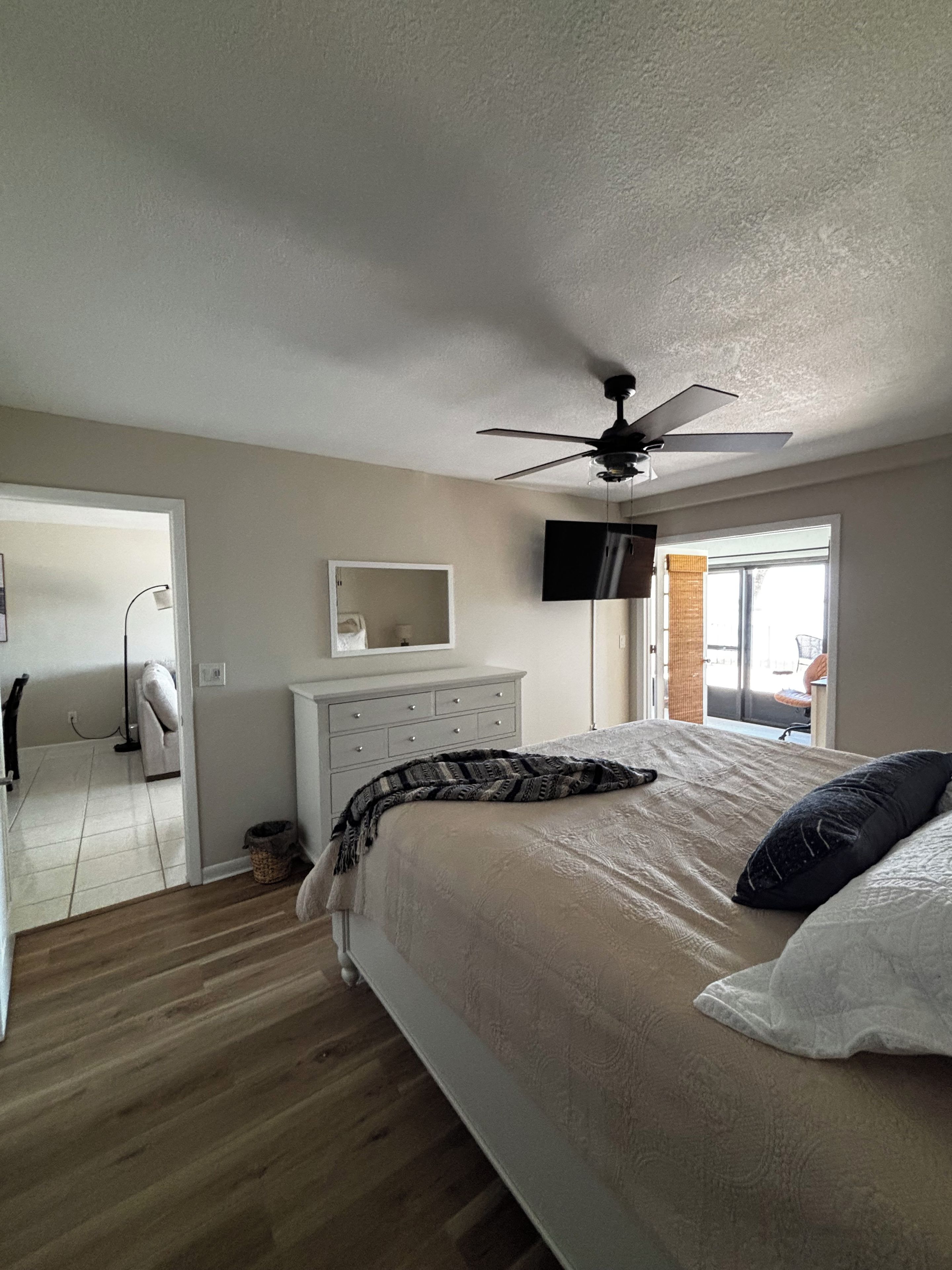 Une chambre à coucher avec un lit, un ventilateur de plafond, une commode, un téléviseur et une fenêtre.