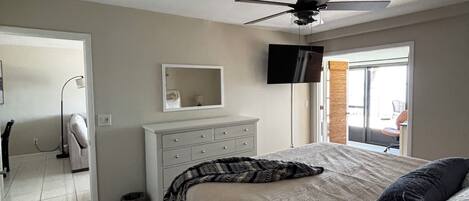 Un dormitorio con cama, ventilador de techo, cómoda, televisor y ventana.
